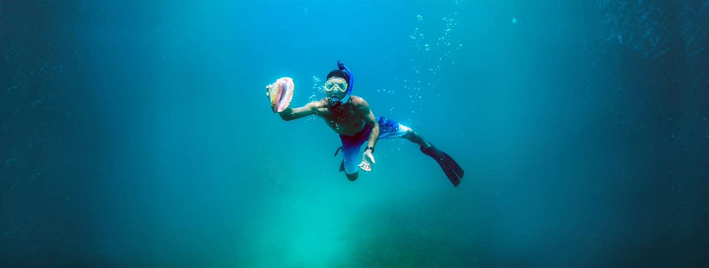 A Watermark Belize Hotel guest holds a conch shell while snorkeling in San Pedro Ambergris Caye